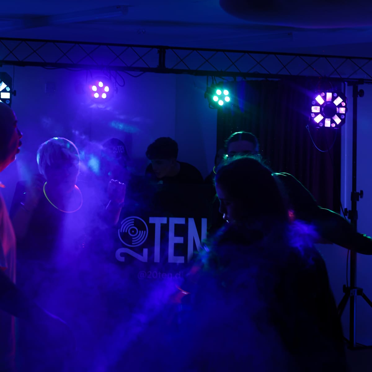 Guests dancing in front of the 20TEN DJ booth under purple lights