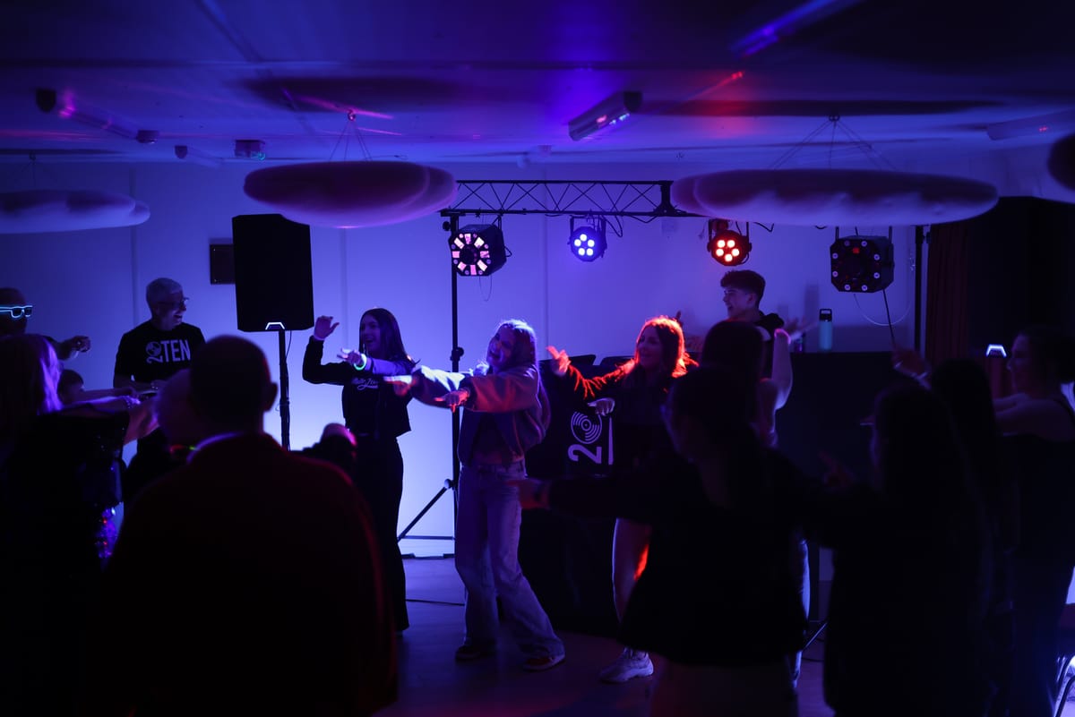 A crowd dancing in front of the 20TEN DJ booth under blue and green lights
